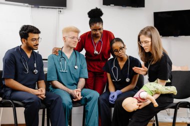 Çeşitli tıp öğrencileri, bir sınıftaki eğitim sırasında tıbbi bir manikinde bebek suni teneffüs yapıyor.
