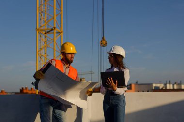 İnşaat işçileri, arka planda vinç olan bir inşaat alanının planlarını inceliyor ve proje planlarını tartışıyorlar.