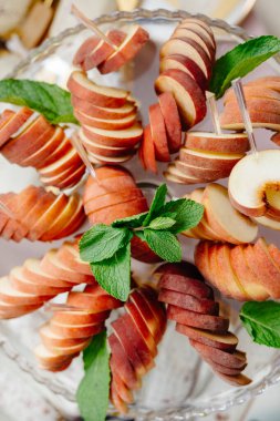 Şeftali dilimleri, cam bir tabaktaki nane yapraklarıyla sarmal bir şekilde düzenlenerek zarif ve ferahlatıcı bir sunum oluşturur.