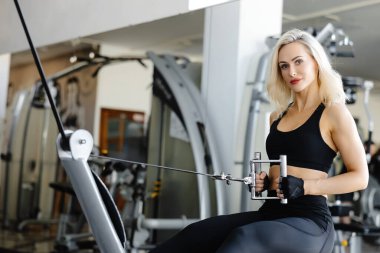 Güçlü bayan sporcu spor salonunda kablo yayını kullanarak sırt kaslarını çalıştırıyor. Sağlıklı yaşam tarzına olan bağlılığını ve gücünü gösteriyor.