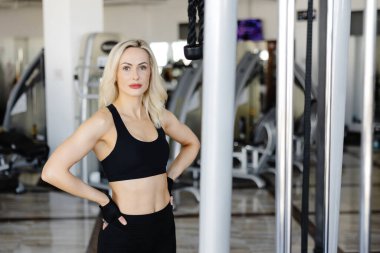 Spor salonundaki antrenman aletlerinin yanında kendinden emin duran genç sporcu, vücut bulmuş ve spor yolculuğuna kendini adamış.