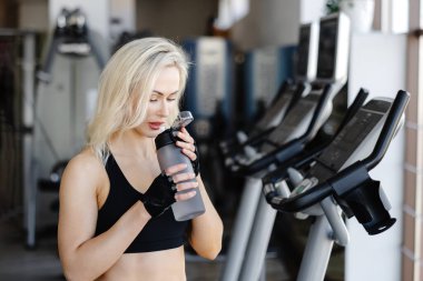 Spor salonundaki yoğun egzersizden sonra ferahlatıcı bir su içen genç sporcu kadın sağlıklı ve aktif bir yaşam tarzını benimsiyor.
