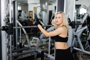 Sarışın sporcu kadın modern fitness merkezinde ağırlık egzersizi yapıyor, bacak ve sırt kaslarını çalıştırıyor.