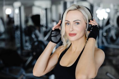 Genç sporcu kadın spor salonunda spor yaparken müziğin keyfini çıkarıyor. Spor kıyafetleriyle enerji ve motivasyon saçıyor.