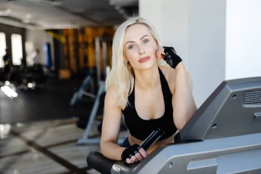 Modern bir spor salonunda koşu bandında kardiyo eğitimi alan atletik bir kadın, spor ve sağlıklı yaşama bağlılığını gösteriyor.