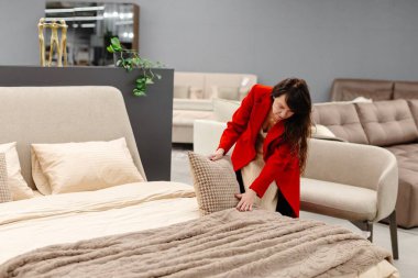 Profesyonel tasarımcı mobilya mağazasında bej bir battaniyeyle yatakta yastık ayarlıyor.