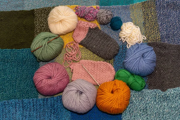 Variety of balls of wool for crochet and knitting on a warm, knitted background with woolen slippers in the making in the middle