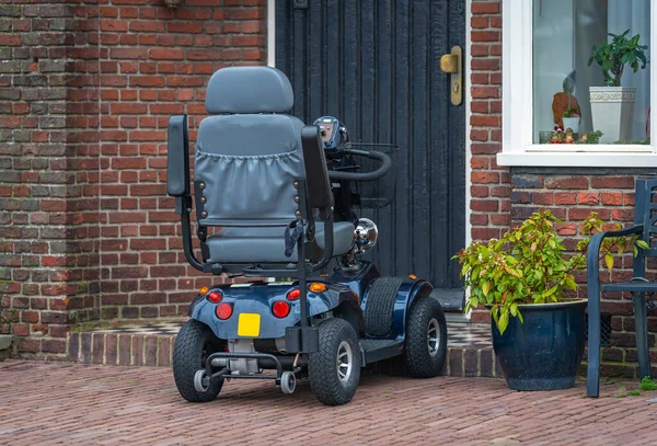 Four wheel mobility scooter parked in front of the house, a modern mobility aid vehicle in the street