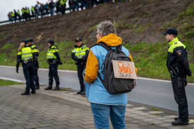 Amsterdam, The Netherlands, 30.03.2024, Elderly climate activist with caricature of The ING Group logo on the backpack during protest action of Extinction Rebellion movement clipart