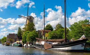 Gouda şehri, Hollanda 'da. Güneşli bir yaz gününde kanalın kenarındaki tarihi yel değirmeni manzarası