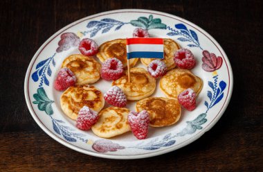 Poffertjes, also called as mini pancakes, with raspberries and powdered sugar on a plate, decorated with dutch flag clipart