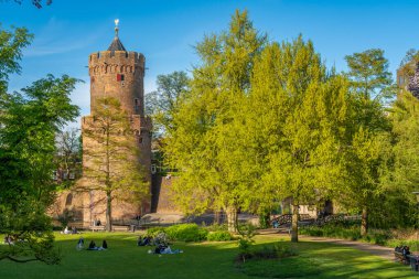 Nijmegen, Hollanda, 19.04.2025, İnsanlar Kruittoren tarihi kulesi manzaralı Kronenburger şehir parkında güneşli bir öğleden sonranın tadını çıkarıyorlar.