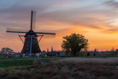 Idyllic Peyzaj 'da Portakal Bulutları ve Söğüt Ağacı ile Sunset' te geleneksel Hollanda Yel Değirmeni