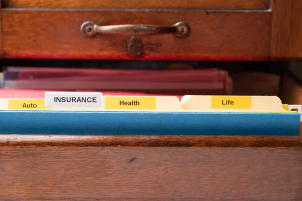 File folders with insurance, auto, health, and life tabs in an antique file drawer.