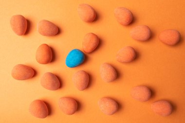 Kalabalığın kavramsal geçmişinde eşsiz ol. Turuncu renkli bir yüzey üzerinde turuncu şekerlerle çevrili tek bir parlak mavi şeker..