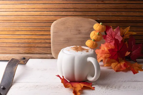 Pumpkin spiced coffee with a stack of tiny pumpkins, autumn leaves and a rustic cutting board.