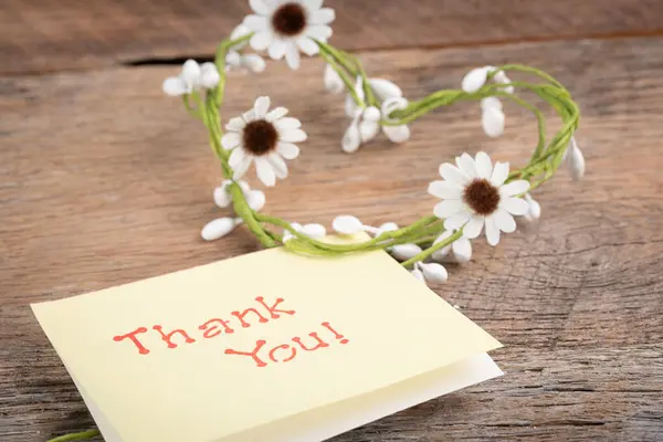 Thank you! on a note card with a heart shaped daisy chain.  Wooden background.