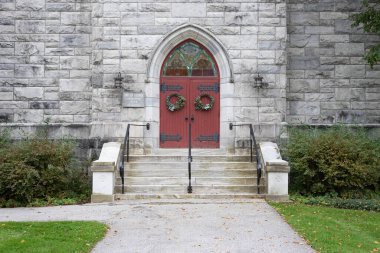 Taştan kilisenin kemerli girişine giden taş basamaklar. Kırmızı kapılar, işlenmiş demir ve boyalı camlar. Birleşik Dorset Kilisesi, Dorset, Vermont, ABD - 23 Eylül 2023. 