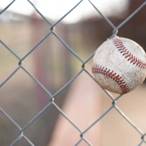 Baseball field background.  Baseball in chain-link fence with soft focus dug-out bench in background.  Baseball field background.