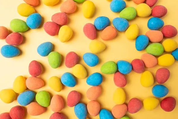 Background image with blue, red, yellow, green, and orange candies on a bright yellow colored surface.