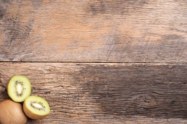 Kivi meyvesi ikiye bölünmüş ve bir tane de ahşap arka planda..