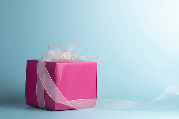 Gift wrapped in bright pink paper with a white bow, on a blue background.