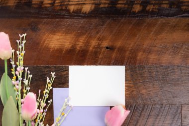 Açık mor zarf ve ahşap zemin üzerinde pembe ve beyaz laleler olan metnin için boş beyaz kart..