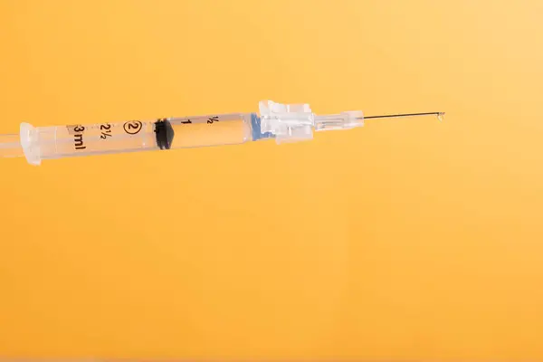 Medical syringe and needle with fluid dripping out of needle.