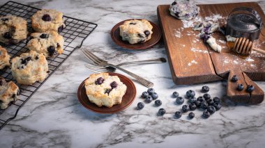 Taze pişmiş yabanmersinli bisküviler, çörekler, mermer arka plan, ahşap kesim tahtası ve tabaklar..