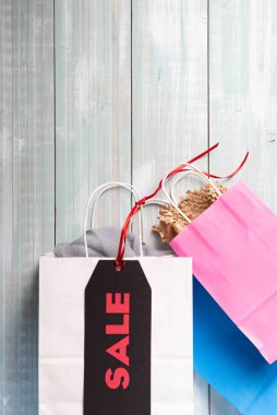 Siyah ve kırmızı etiket. Açık mavi tahta arka planda beyaz, mavi ve pembe alışveriş torbaları..