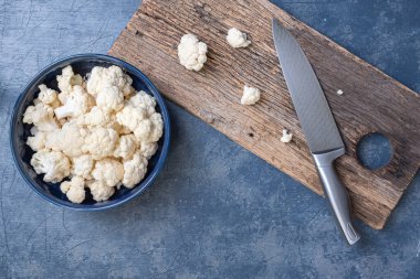 Taze kesilmiş mavi kase sağlıklı beyaz karnabahar ahşap kesim tahtası ve mavi arka planda bir bıçakla.