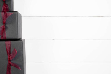 Alışveriş, bağış ya da Kara Cuma indirimi konsepti. Siyah kağıda sarılı, beyaz tahta arka planda kırmızı kurdeleli bir sürü hediye..