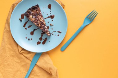 Parlak sarı bir yüzey üzerinde mavi tabakta karamel, çikolata, çikolata ve ceviz ile cheesecake.