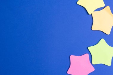 Boş, yıldız şekli renkli, parlak mavi arkaplan üzerine kağıt bloknotlar, boşluğu kopyala.
