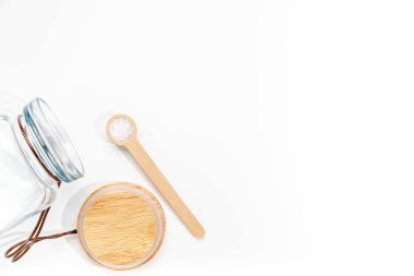 Tahta kaşıkta deniz tuzu, beyaz arka planda bambu kapaklı cam kavanoz..