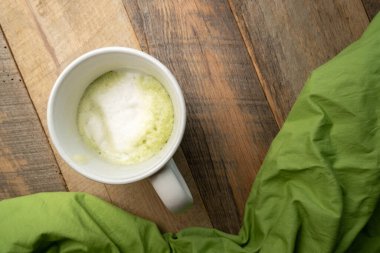 Sıcak, yeşil çay latte evde, üst manzara, ahşap masa üzerinde parlak yeşil bir peçete.