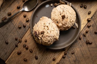 İki kepçe gurme kahve aromalı ev yapımı dondurma koyu kahverengi sığ kase, ahşap masa, etrafa dağılmış kahve çekirdekleri..