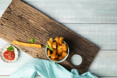 Ev usulü patates kızartması, ketçaplı ve çiftlik soslu mavi bir kasede, kırsal kesim tahtasında..