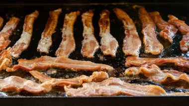 Domuz pastırması, dökme demir ızgarada cızırdıyor ya da üstü düz ızgara, açık hava kampı pişirme, yakın çekim.