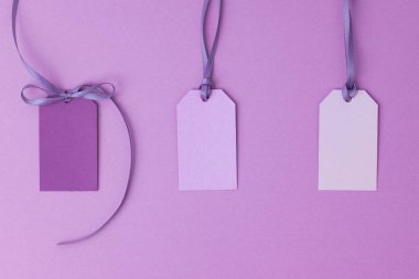 Menekşe mor yüzey üzerinde kurdeleli üç boş hediye etiketi veya etiket.