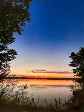 Su, gökyüzü, ağaçlar ve çalılarla güzel bir günbatımı