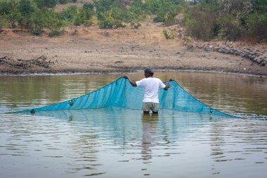 TIKAMGARH, MADHYA PRADESH, Hindistan - 21 AĞUSTOS 2023: Küçük bir gölde balık yakalayan bir adam.