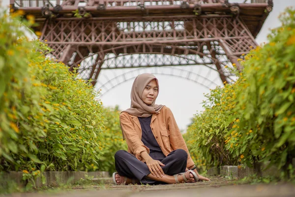 花の庭の道の真ん中に座っている現代のヒジャーブ服の美しいイスラム教徒のアジア人女性 — ストック写真