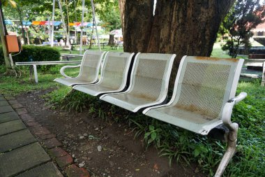 Üzerinde kimsenin oturmadığı paslı, beyaz bir demir park bankı.