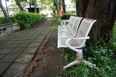 Üzerinde kimsenin oturmadığı paslı, beyaz bir demir park bankı.