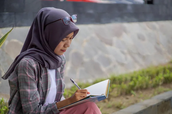 Modern Başörtüsü Takan Güzel Asyalı Müslüman Kadın Kitabında Oturuyor Yazıyor — Stok fotoğraf