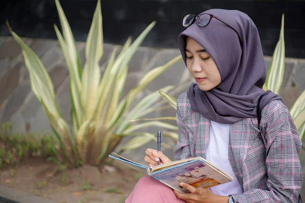 美しいアジア系ムスリム女性は 現代のヒジャーブを身につけて本に書いています — ストック写真