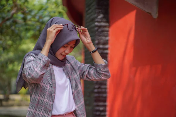 美しいですアジアのイスラム教徒身に着けています現代のヒジャーブ人女性と手ポージング保持眼鏡で彼女の頭の上に公園 — ストック写真