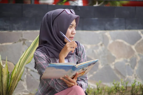 本とペンを持った美しいアジア系イスラム教徒のヒジャーブ人女性です イスラム教徒の女性が何かを書くことを考える本を持っていて — ストック写真
