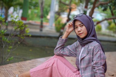 Güzel Asyalı Müslüman kadının modern tesettüre binmiş parkta otururken çekilmiş bir fotoğrafı.